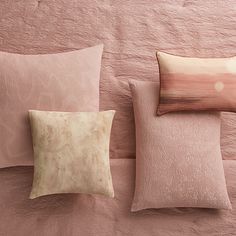 three pillows and two pillow cases on a bed with pink linens, one in the shape of a rectangle