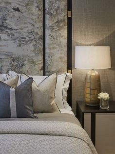 a bed with many pillows on it next to a night stand and lamp in the corner