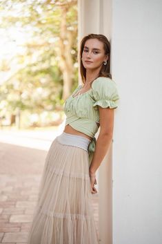 a woman is leaning against a wall wearing a skirt and crop top with her hands on her hips