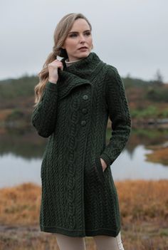 a woman standing in front of a body of water wearing a green coat