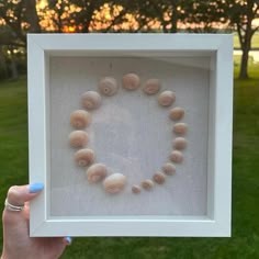 a person holding up a frame with shells in the shape of a heart on it