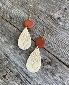 two white and red earrings with flower design on the front, sitting on a wooden surface