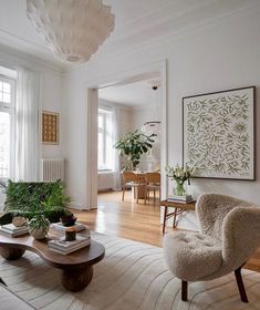 a living room filled with lots of furniture and plants on top of a hard wood floor