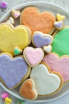 a plate full of heart shaped cookies on top of a white tablecloth with candy candies