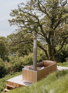 a wooden hot tub sitting on top of a lush green hillside next to a tree