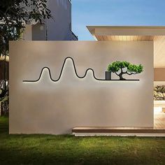 a white wall with a tree and plant on it in front of a modern house