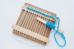 the loom is made out of cardboard and string with two blue pins on it