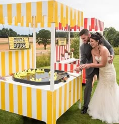 a newly married couple cutting their wedding cake in front of an ice cream stand with striped yellow and white stripes