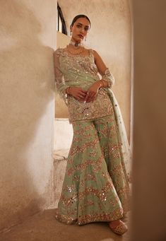 Dive into elegance with this mesmerizing sea green raw silk sharara set. The fully embroidered kurta, adorned with resham, mirror, sequin, and zardosi embroidery, exudes opulence and charm. Paired with a chevron sharara, this ensemble offers a perfect blend of traditional craftsmanship and contemporary design. Embrace sophistication and make a statement with this timeless piece. Raw Silk Sharara, Bridal Gharara, Green Sharara, Silk Sharara, Mirror Sequin, Embroidered Sharara, Mehendi Outfit, Zardosi Embroidery, Bride Sister