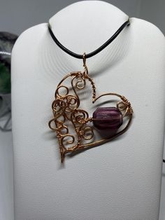 a heart shaped pendant on a white display stand with a purple bead in the middle