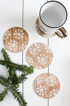 three wooden coasters with snowflakes on them next to a mug and pine branch