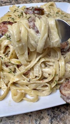 a white plate topped with pasta covered in sauce and meats next to a fork