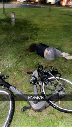 a man laying on the ground next to a bike and another person lying in the grass