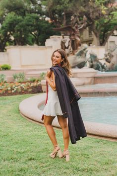 a woman standing in front of a fountain wearing a black and red graduation robe with her hand on her hip