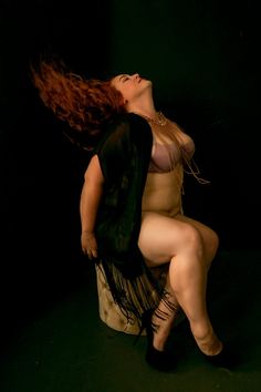 a woman with long red hair sitting on top of a stool in a dark room