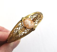 "Antique art deco cameo bracelet. The hinged bangle bracelet is a gold wash over ornate stamped metal and filigree. A small pink shell cameo of a woman's profile is the prong set focal. The unusual clasp features a very long tongue that slides along the interior of the bracelet. Size: Interior diameter of the bracelet is 7\". The width is 3/4\" at its widest and 1/4\" at its narrowest. The cameo is 1/2\" x 3/8\". Condition: Excellent antique condition. The clasp opens and closes securely. There Art Deco Shell, Cameo Bracelet, Stamped Metal, Gold Wash, Antique Art Deco, Hinged Bangle, Antique Art, Bangle Bracelet, Prong Setting