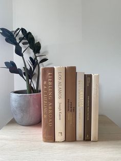 three books sitting on top of a wooden table next to a potted plant