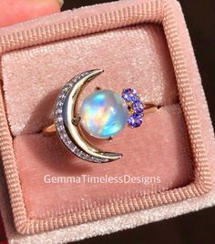 This new galaxy design is a gorgeous natural diamond, moonstone and tanzanite ring, it is perfect for an engagement ring or just a beautiful gift to someone special. The ring is made with 14K solid yellow gold, features a high quality cabochon moonstone (2.00ct, 8mm), side diamonds (approx 0.15ct total weight, Si clarity), natural tanzanites ( 0.12ct, vs clarity). Ring is in size 8.   **All our products will come with a certificate of authenticity provided by The Valuation Centre of Australia wh Celestial Style Opal Ring, Moonstone Multi-stone Opal Ring As Gift, Multi-stone Moonstone Opal Ring For Gifts, Celestial 14k Gold Moonstone Ring For Gift, Celestial 14k Gold Moonstone Ring As Gift, Celestial Style 14k Gold Moonstone Ring As Gift, Celestial Moonstone Ring In 14k Gold As Gift, Celestial Opal Ring As Gift, Celestial Style Opal Gemstone Ring