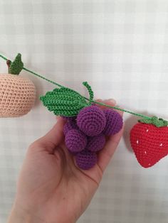 crocheted fruits and vegetables are hanging on a clothes line, with one hand holding the string