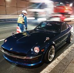 a man standing next to a blue sports car on the side of a city street