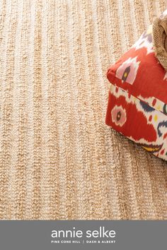 an area rug with a red flowered pillow on top of it and the words annie selke written in white