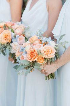 two bridesmaids holding bouquets of peach and blue flowers in their hands,