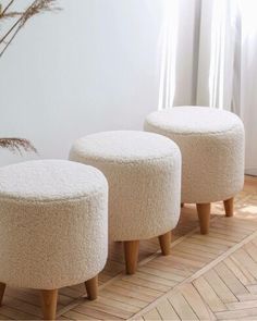 three white stools sitting next to each other on top of a wooden floor in front of a window