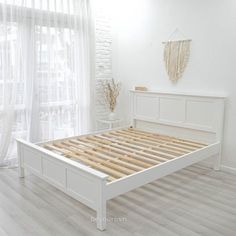 a white bed frame with wooden slats in a bright room, next to a window