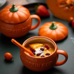 there is a bowl of soup with strawberries on the table next to two orange pumpkins