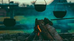 an outdoor fire pit with hanging pots over it and logs in front of the fire