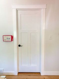 an empty room with a white door and wooden floor in front of the door is a clock on the wall