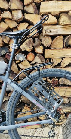 a close up of a bike parked next to a pile of firewood with logs in the background