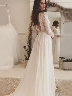 a woman standing in front of a mirror wearing a white wedding dress with long sleeves