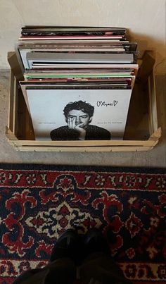 a person standing in front of a pile of records on the floor next to a rug