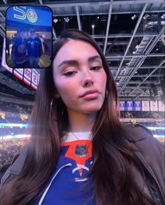 a woman with long brown hair is taking a selfie in front of an arena