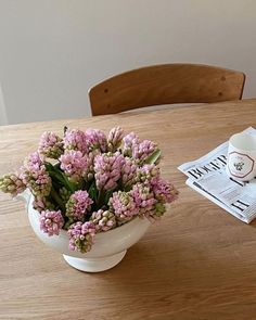 a wooden table topped with a white vase filled with pink flowers next to a newspaper