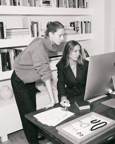 two women looking at a computer screen in front of a bookshelf full of books