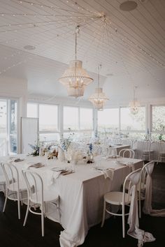 a dining room with tables and chairs covered in white linens, lights strung from the ceiling