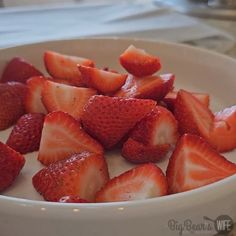 a white bowl filled with sliced strawberries on top of a table