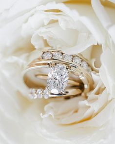 two wedding rings sitting on top of a white peonie flower with the petals blooming