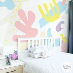 a white bed sitting under a colorful wall mural