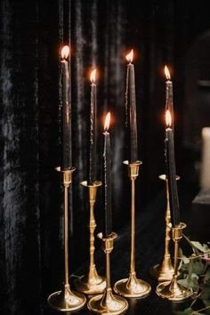 four candles are lit on a table with greenery