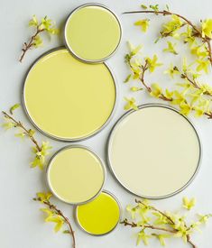 three paint cans with yellow and white paint sitting on top of each other next to flowers