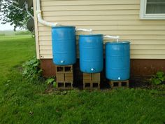 three large blue barrels sitting in front of a house next to a green yard and grass