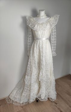 Long wedding gown from 89s in victorian style. Frills in top and bottom. Flower lace all over the dress. In waist white ribbon. On the back bow, zip fastener, medium long tail. Size rather XS but please check belowe. Measurement taken flat and doubled: Bust 82 cm Waist 62 cm Lenght im front 134cm Vintage Ruffled Dress For Debutante Ball, Lace Gown With Ruffles For Debutante Ball, Lace Ball Gown With Ruffles, Long Sleeve Lace Dress For Wedding, Cream Lace Vintage Dress With Ruffles, White Vintage Victorian Ball Gown, Elegant Vintage White Victorian Dress With Ruffles, Vintage Victorian Dress With Ruffles For Debutante Ball, Long Sleeve Victorian Dress With Ruffles For Vintage Events