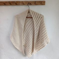 a crocheted shawl hanging from a coat hook on a white wall next to a wooden hanger