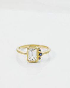 a gold ring with an emerald and blue sapphire stones in the center on a white background