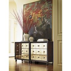 an ornate dresser with drawers and vases in front of a painting on the wall