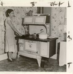 an old black and white photo of a woman standing in front of a stove with pots on it