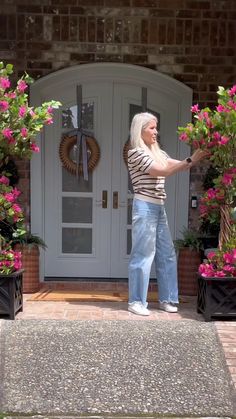 a woman standing in front of a white door with pink flowers on the side walk